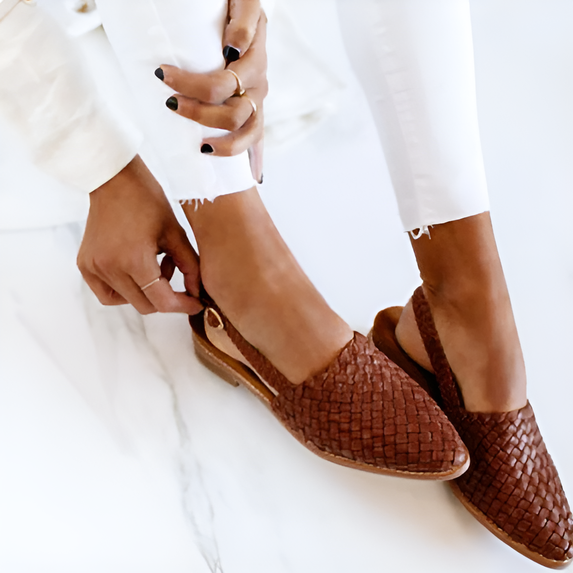 Vrouw draagt bruine gevlochten leren loafers, stijlvolle casual schoenen, op een witte marmeren vloer. Trendy damesmode, comfortabele schoenen.