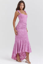 Vrouw in elegante roze kanten jurk met asymmetrische zoom, staand op hakken. Perfect voor avondkleding, bruiloften en speciale gelegenheden.
