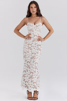 Vrouw in elegante witte kanten jurk met bloemenpatroon, spaghetti bandjes en aansluitende pasvorm. Perfect voor bruiloften en formele evenementen.