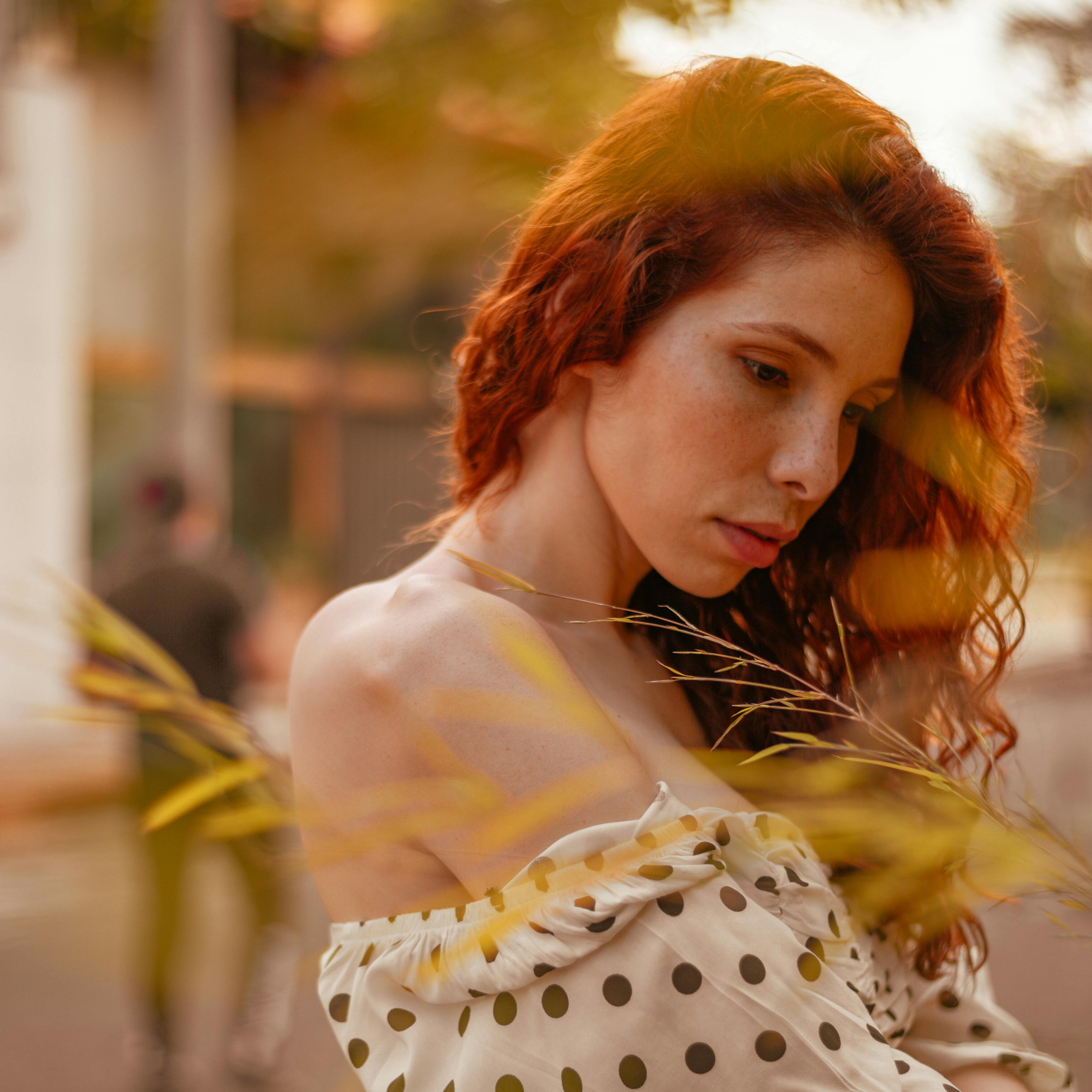 Roodharige vrouw in stippenjurk, buiten in zonlicht. Natuurlijke schoonheid, zomerse sfeer, modefotografie, portret, zachte focus.